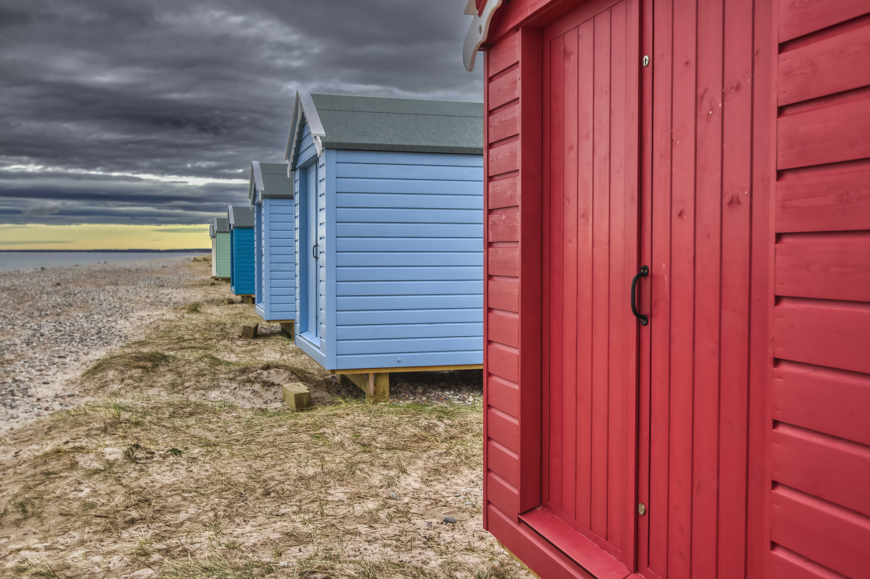 Brightly painted beach huts against a moody sky at Findhorn Bay